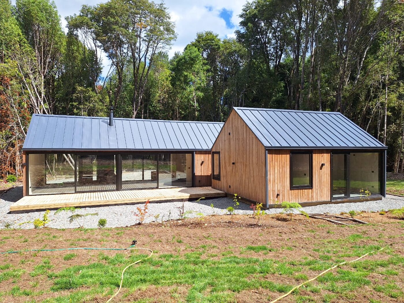 Casa de madera con techo a dos aguas y ventanales corridos, rodeada de bosque en Puerto Varas