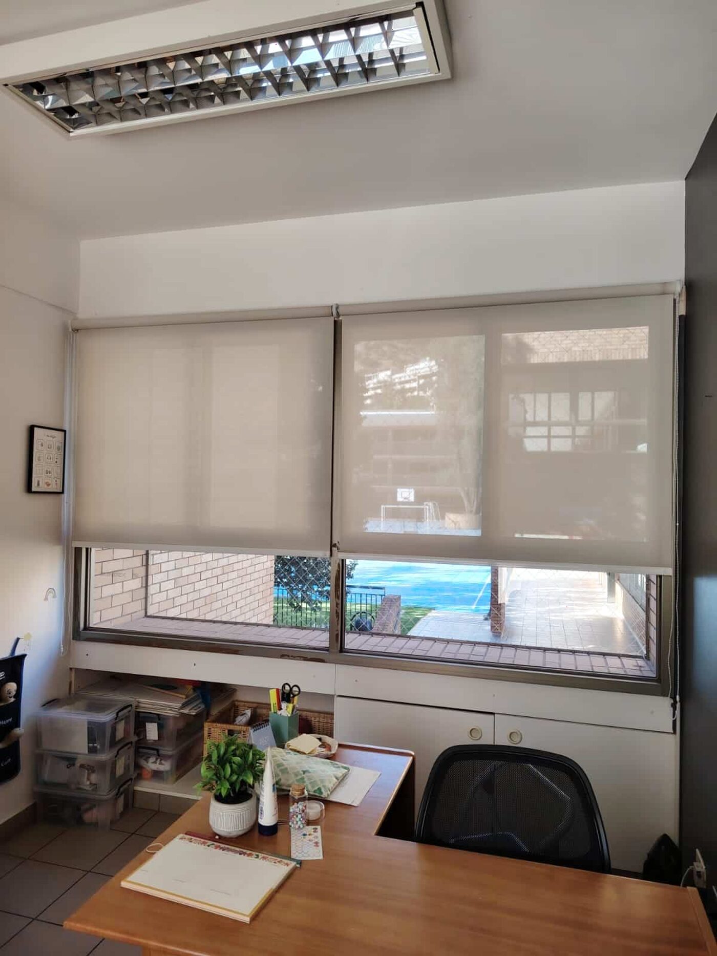 Oficina del colegio con cortina roller sobre la ventana y escritorio de madera
