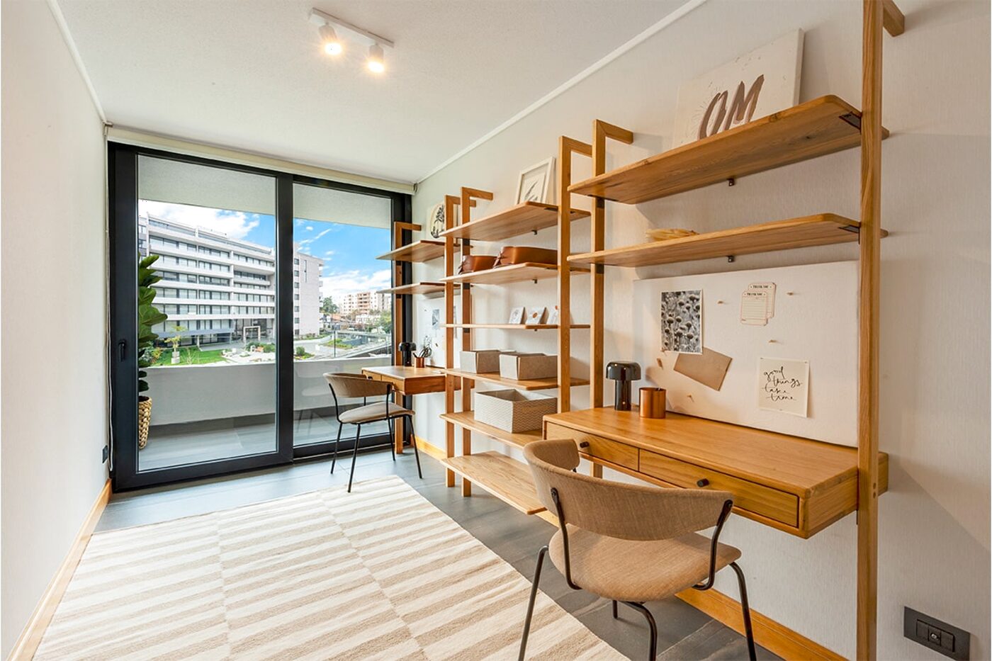 Escritorio y estantería junto a un ventanal con cortina roller, con vista al conjunto