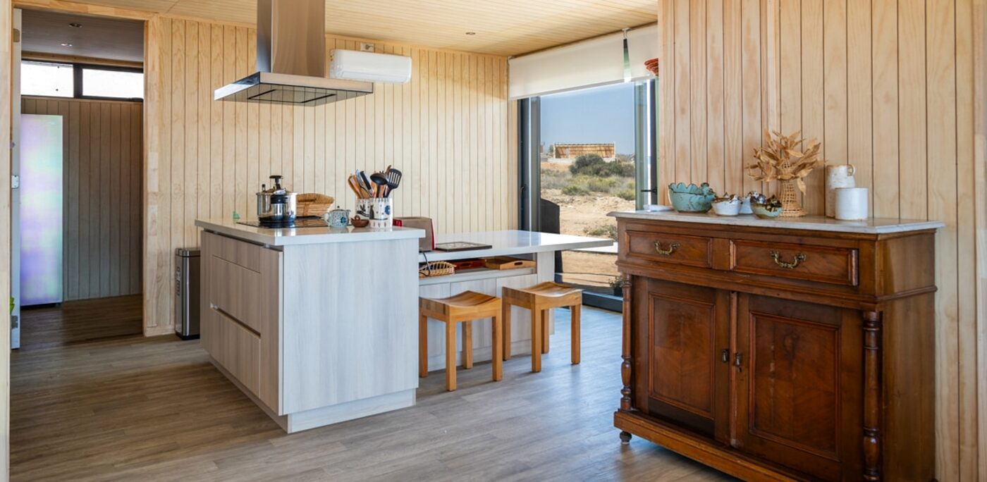 Cocina con isla central y comedor, muros de madera clara y ventanal al patio