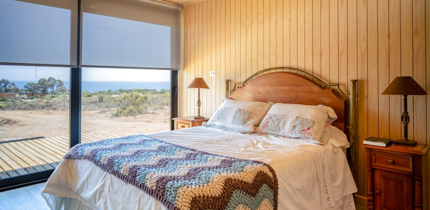 Dormitorio con cortina roller sobre el ventanal, con vista al exterior