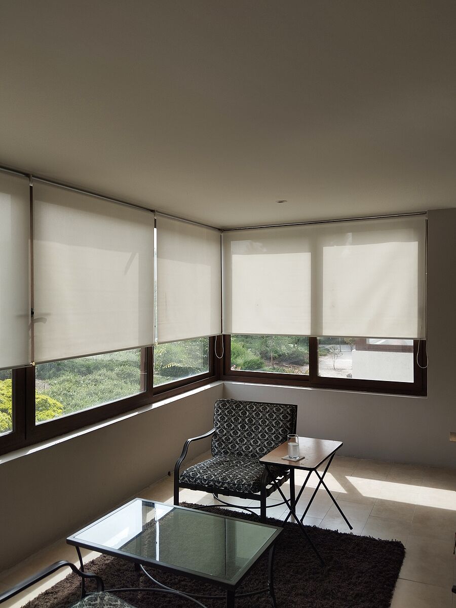 Cortinas roller sunscreen en living comedor con ventanas en esquina y vista al jardín