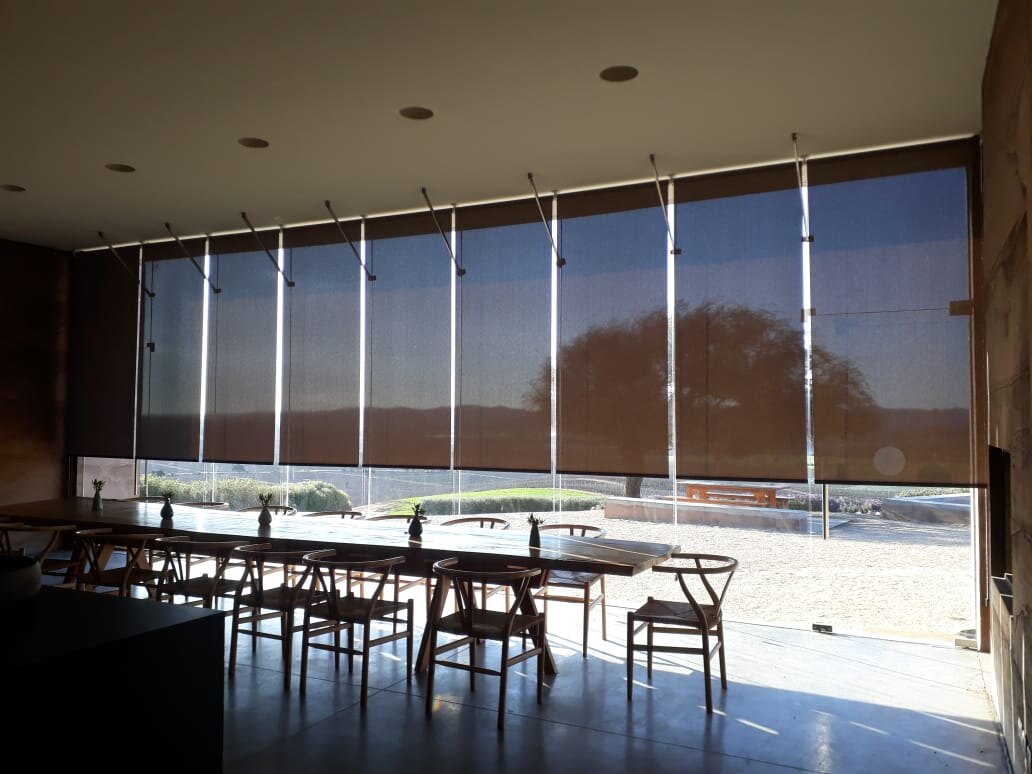 Ventanal completo con cortinas roller a medida sobre una mesa larga de comedor